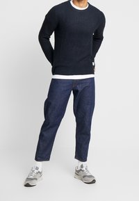 Marinblå stickad tröja med mönstrad textur, vit krage, kombinerad med mörka jeans och grå sneakers. Avslappnad, löstsittande passform.