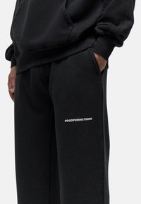 Zwarte trainingsbroek met een losse pasvorm, gemaakt van zacht materiaal. Bevat een witte "GOODFOR NOTHING" graphic op de linker bovenbeen en zijzakken.