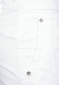 Bílá deninová tkanina s jemnou texturou, která obsahuje zakřivený design kapsy, zesílené švy a akcenty v podobě stříbrných cvočků.