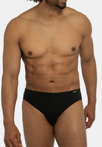 Slip in stile bikini nero realizzato in un materiale liscio. Presenta un design minimal con una cintura elastica standard e senza motivi.