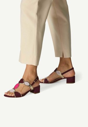 Sandales à talon carré avec un design bordeaux et or métallique. Présentent des accents circulaires en rose, blanc et violet. Fermeture à bride autour de la cheville.