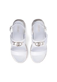 White sandals featuring a smooth synthetic upper, wide front straps, adjustable ankle strap, and a silver buckle detail. Thick sole.