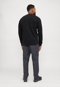 Zwarte lange mouw shirt met een gestructureerde afwerking, gecombineerd met grijze cargobroek met meerdere zakken en zwarte schoenen.