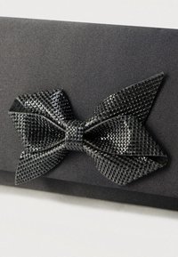 Fekete táska texturált felülettel, nagy, fényes fekete flitteres masnival díszítve. Simább anyag, elegáns kialakítás.