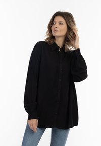 Zwarte langek-mouw shirt met een knoopsluiting aan de voorkant, zachte textuur en verzamelde manchetten, gecombineerd met lichtblauwe jeans.