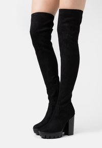 Černé semišové kozačky nad kolena, s robustním podpatkem, bočním zipem a hladkou texturou. Klasický design s přiléhavým střihem.