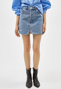 Denimminikjol med en frontslits, fransade kanter och ljusblå färg. Matchas med svarta ankle boots och en långärmad blå- och vitrandig skjorta.