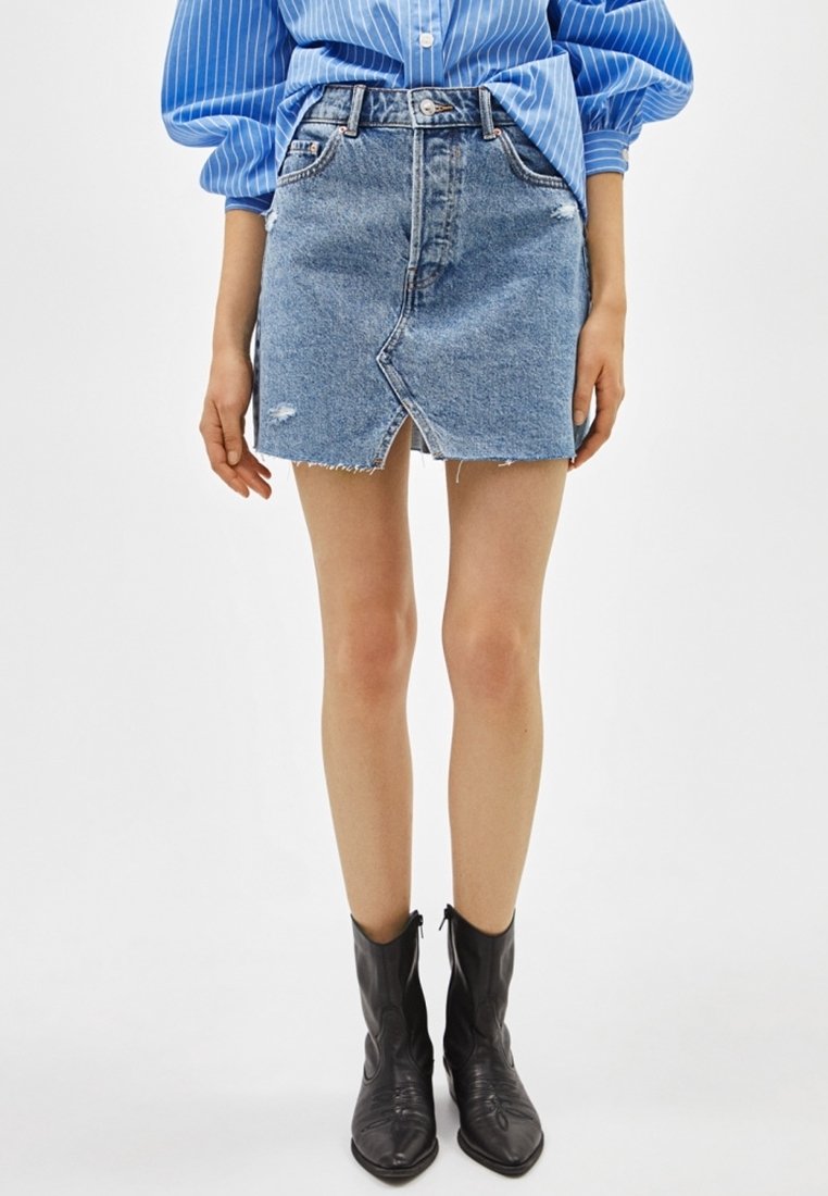 Denimminikjol med en frontslits, fransade kanter och ljusblå färg. Matchas med svarta ankle boots och en långärmad blå- och vitrandig skjorta.