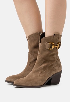Botas de tobillo de ante marrón con punta afilada, diseño esculpido y un hebilla de acento dorado en el lateral. Tacón mediano apilado.