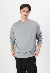 Sudadera gris confeccionada en tela suave, con cuello redondo y hombros caídos. Lleva bordado en negro "no desperdicies la cultura" en el pecho.