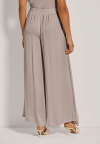 Lichtbeige wijde broek met een elastische tailleband, gemaakt van een zachte, gestructureerde stof, met een vloeiende uitstraling die elegant valt.