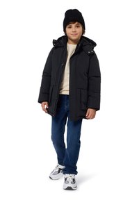 Giacca a palloncino nera con cappuccio, tessuto strutturato, due tasche frontali, indossata sopra un maglione crema, abbinata a jeans blu e sneakers.