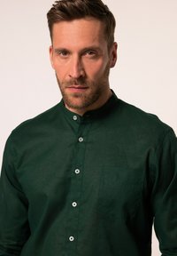 Donkergroene blouse met knopen, gemaakt van een textuurstof, met een kraag, een borstzak en zilveren knopen aan de voorkant.