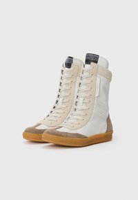Sneaker alta color beige chiaro in pelle liscia, con dettagli in suede, particolari perforati e suola in gomma. I lacci si estendono fino alla parte superiore.