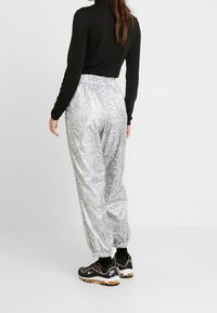 Silver- och svartmönstrade joggers med elastisk midja, tillsammans med svarta träningsskor med färgglada accenter och en texturerad sula.