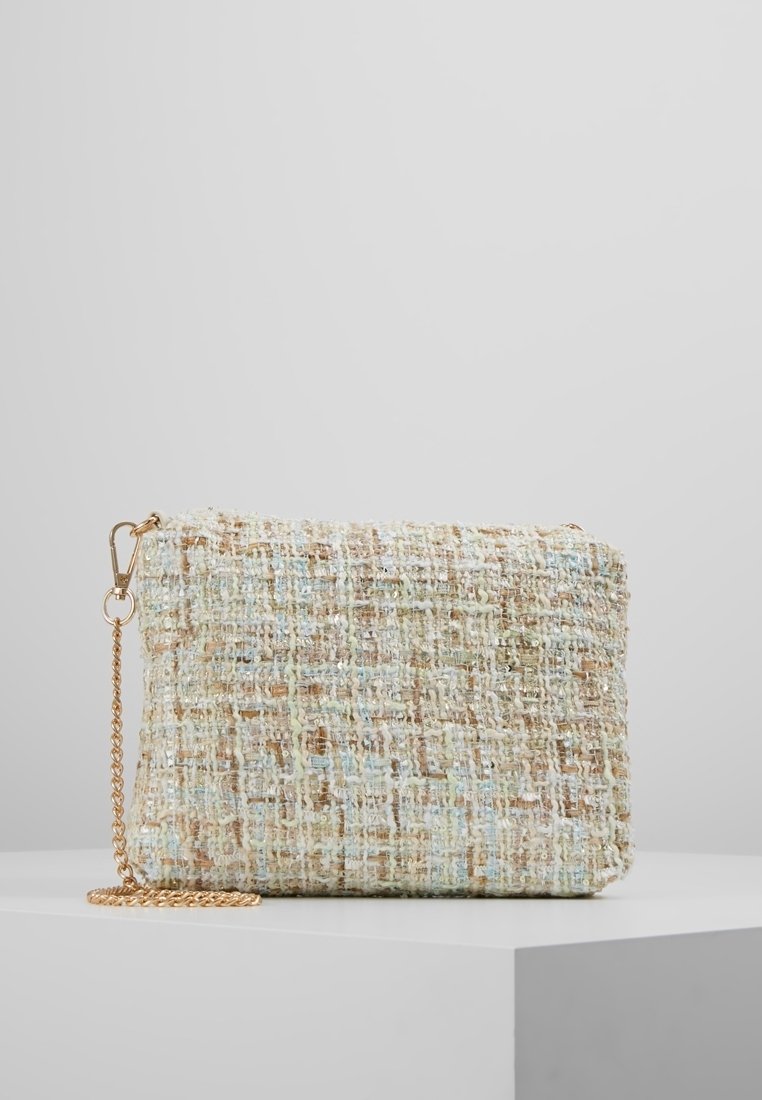 Pochette rectangulaire en tweed avec des fils beige, bleu et blanc, dotée d'une bandoulière chaîne dorée, posée sur une surface blanche sur fond gris.