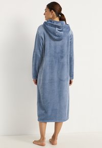 Hoodad rock i mjukt, ljust blått fleece, med en lång design som når till mitten av vaden, långa ärmar och en slät textur.
