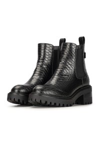 Botas negras de cuero hasta el tobillo con un patrón de piel de serpiente texturizada, paneles laterales elásticos y una suela gruesa y dentada. Notables tiradores en la parte posterior.