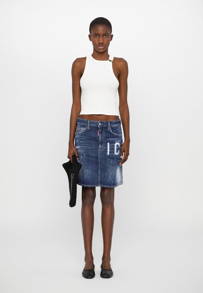 Jeansrock in Dunkelblau mit distressed Details, mittellange Länge bis zur Oberschenkelmitte, mit vorderem Knopfverschluss und großem weißen "IC"-Druck. Kombiniert mit einem figurbetonten weißen Tanktop.