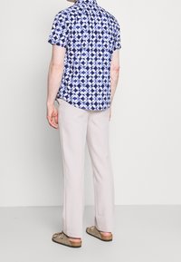 Korte mouw shirt met een blauw-wit geometrisch patroon, gecombineerd met lichtbeige broeken en taupe sandalen met banden.