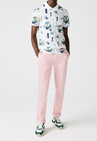 Polo blanc à manches courtes avec des motifs de plantes colorés, associé à un pantalon rose clair et des baskets à accents verts. Tissu doux, coupe décontractée.