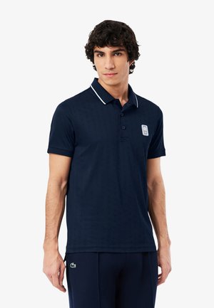 Marineblauw poloshirt met korte mouwen, reliëfpatroon en witte kraagaccenten. Voorzien van een geborduurd logo op de borst.