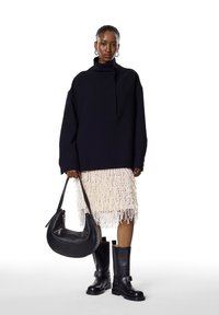 Pulover negru supradimensionat, fusta albă cu franjuri, cizme negre din piele până la genunchi și o geantă neagră cu accente argintii. Design minimalist.