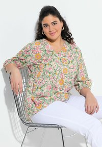 Blusa con stampa floreale caratterizzata da scollatura a V, maniche 3/4 e vestibilità rilassata. I colori includono verde, rosa, giallo e crema. Abbinala a pantaloni bianchi.