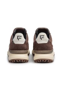 Un paio di sneaker in suede marrone con suole beige viste da dietro, dotate di una toppa grigia e di un logo geometrico nero su ogni tacco.