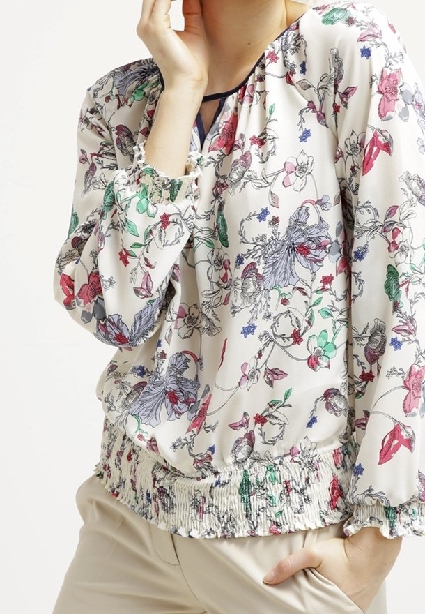 Blommig blus i lätt tyg, med vit bas och färgglada blommönster, elastisk smockad nederkant och rynkade ärmar.