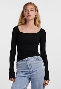 Maglione nero a costine con scollatura quadrata. Abbinato a jeans chiari strappati a vita alta.