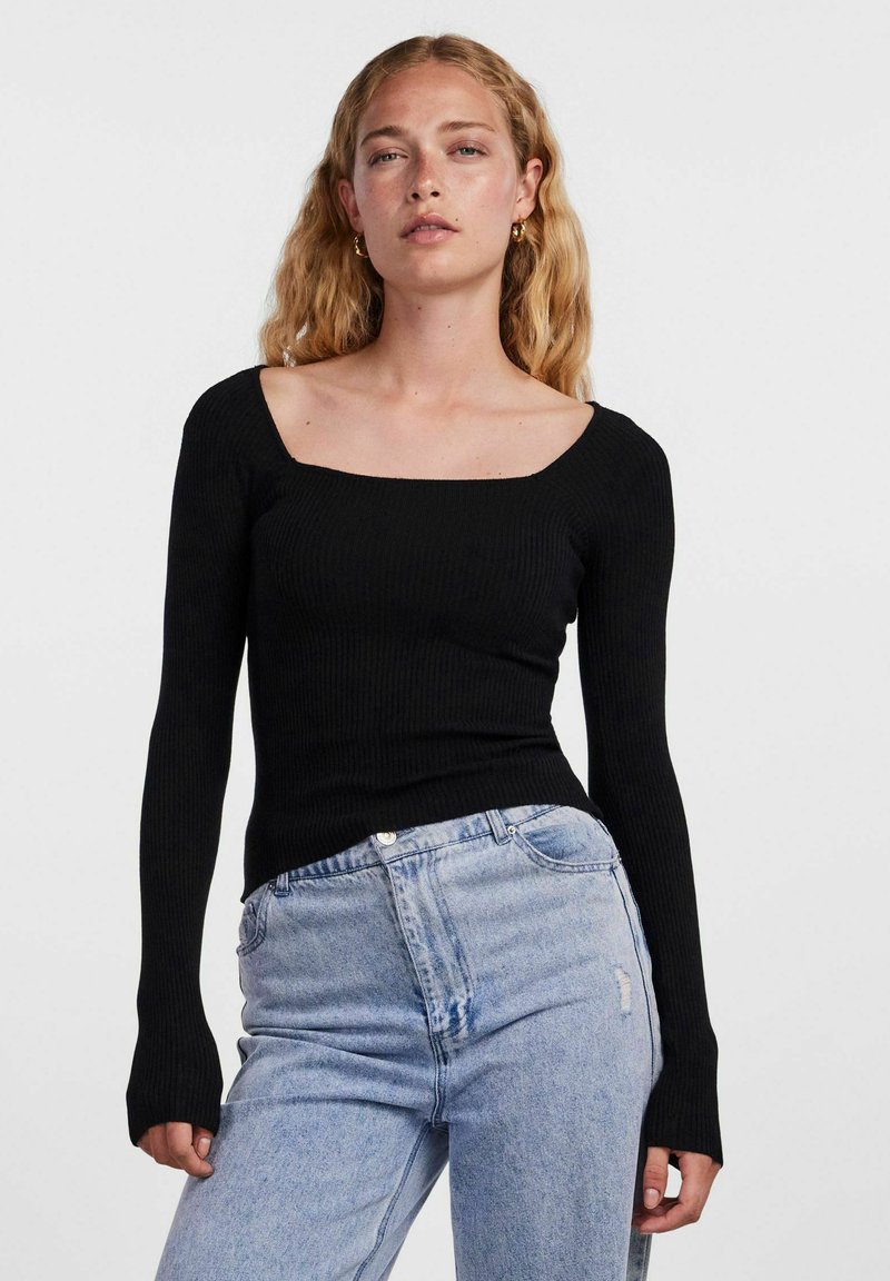 Maglione nero a costine con scollatura quadrata. Abbinato a jeans chiari strappati a vita alta.