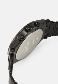Reloj cronógrafo negro con correa de malla, tres botones en el lado derecho, esfera redonda y parte trasera plateada lisa.
