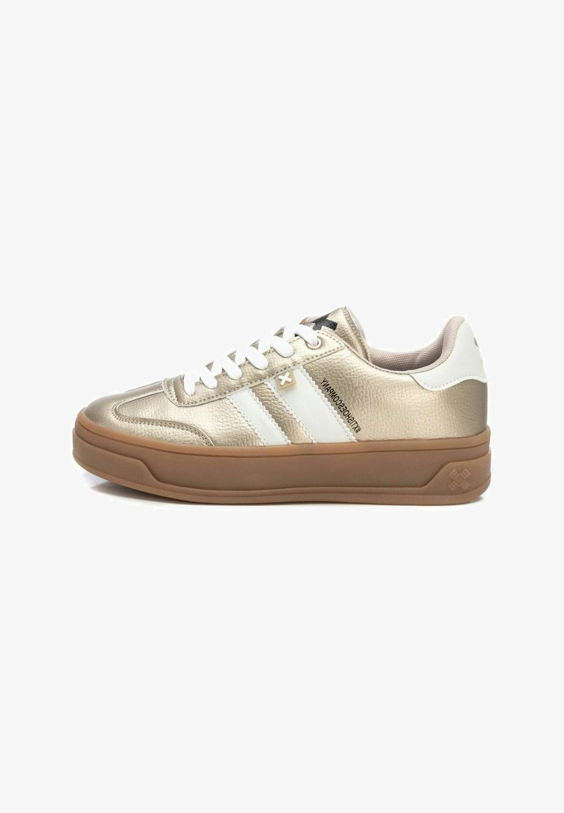 Zapatilla metálica dorada con rayas blancas, punta redonda, cordones blancos, parte superior texturizada y suela de goma. Presenta un logo en la lengüeta.