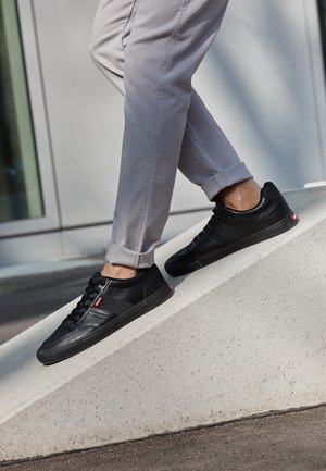 Personne portant un pantalon gris clair et des baskets noires à tige basse marchant sur une rampe en béton à l'extérieur près d'un bâtiment.