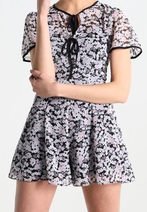 Musta ja vaaleanpunainen kukkakuvioinen haalari, jossa on läpinäkyvä yläosa, lyhyet hihat ja solmittava kaulanauha. Hameessa laskostettu yksityiskohta.