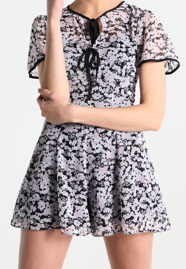 Combinaison fleurie en noir et violet clair avec un corsage transparent, des manches courtes et une fermeture à nouer au niveau du col. Détail de jupe plissée.