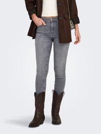 Gray skinny jeans paired with a dark brown suede blazer. Brown cowboy boots feature decorative stitching and a pointed toe.