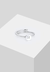 Anillo ajustable de plata con un disco redondo en la parte superior, en el que está grabada la letra "M". Diseño simple con un acabado pulido.