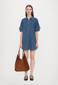 Denim shirtjurk met korte pofmouwen, knoopsluiting en een lichte rafeling aan de zoom. Bruine suède totebag met lange schouderbanden en logodetail.