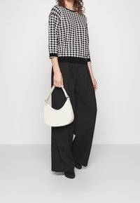 Pull-over pied-de-poule noir et blanc à manches trois-quarts associé à un pantalon large noir. Tient un petit sac blanc de forme incurvée.
