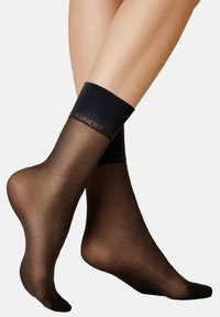 Durchsichtige schwarze Knöchelstrümpfe mit einem verstärkten dunklen Bund oben, der den Markennamen "KUNERT" in subtiler Schrift zeigt.