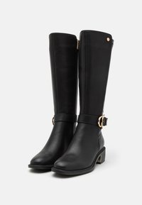 Botas negras hasta la rodilla de cuero suave, con cremallera lateral, un hebilla decorativa y un tacón bajo tipo bloque con acentos dorados.