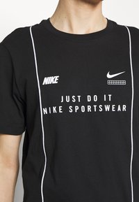Schwarzes Baumwoll-T-Shirt mit weißem "Nike"-Logo, dem Text "Just Do It" und Akzentstreifen an den Seiten. Runder Ausschnitt, kurze Ärmel.