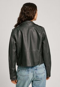 Zwarte leren motorjack met ritsen, gestructureerde schouders en een cropped ontwerp, gecombineerd met blauwe denim jeans.