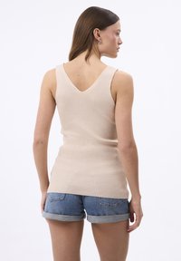 Top senza maniche a coste beige con un design a V sul retro, abbinato a pantaloni corti in denim arrotolati. Tessuto morbido, forma aderente, costruzione semplice.