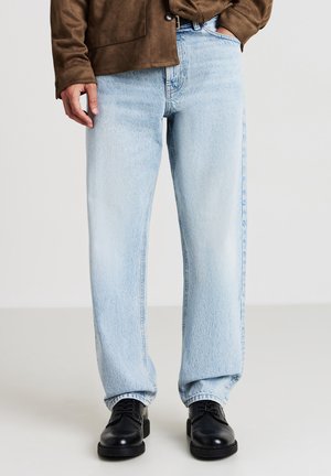 Hellblaue Denim-Jeans mit lässigem Schnitt, hoher Taille und geraden Beinen, kombiniert mit schwarzen Lederschuhen.