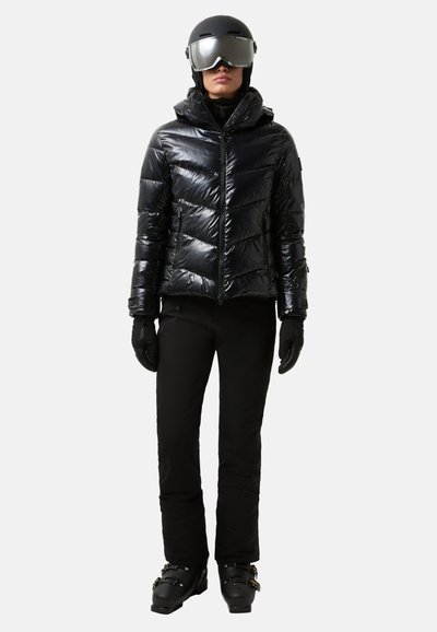 Czarna, błyszcząca kurtka puchowa z przeszyciem w kształcie litery V, w połączeniu z czarnymi rękawiczkami i spodniami narciarskimi. Zawiera kask i lustrzane gogle.