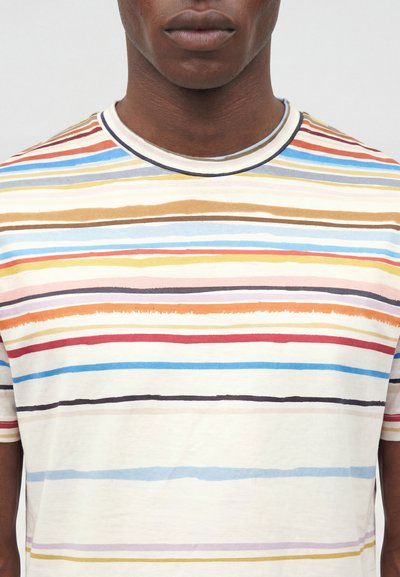 Άνδρας που φοράει κρεμ κοντομάνικη μπλούζα με ακανόνιστες οριζόντιες ρίγες σε μπλε, κόκκινο, κίτρινο, καφέ και πορτοκαλί.