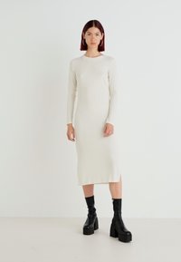 Vestido midi de manga longa em off-white com fendas laterais. Combinado com botas ankle de plataforma pretas. Textura suave.